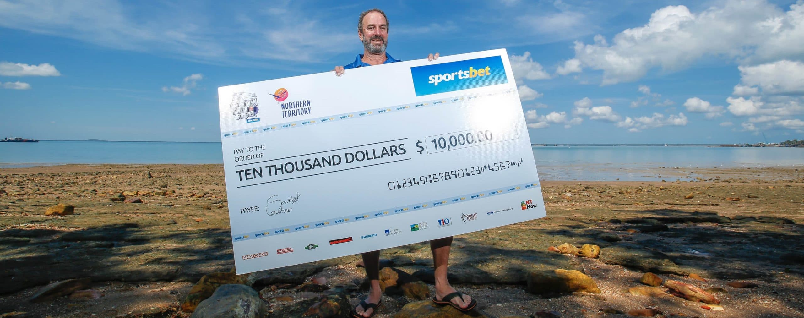 Man holding up $10,000 cheque at beach